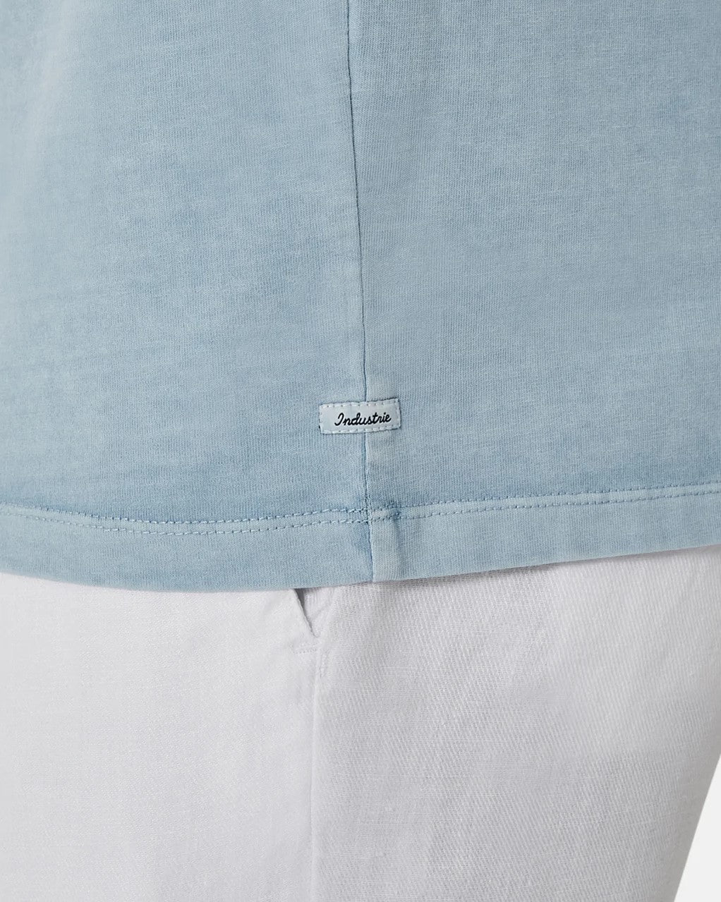 Close-up of a person in an oversized light blue Industrie The Del Sur Tee and white pants, featuring a small tag near the hem that adds a subtle touch to its relaxed style.