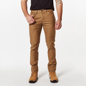 A person wearing a black shirt is showcasing a pair of comfortable, tan-colored Levis Workwear 511 Utility Pants with their hands resting by their sides. They are also wearing tan work boots. The person has a tattoo on their right forearm, with the white background highlighting the stylish Levis Workwear 511 Utility Pant they're sporting.