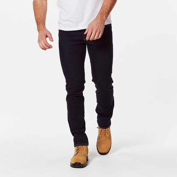 A person wearing dark Levis Workwear 511 Slim Jeans, a white shirt partially visible, and tan work boots with black soles walks toward the camera. The background is a plain white studio setting, highlighting their comfortable yet stylish outfit.