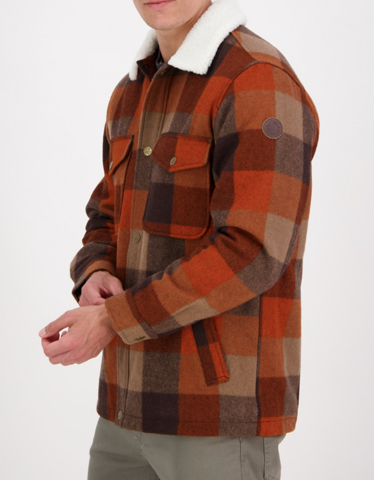 Wearing the Swanndri Kaituna Sherpa Lined Jacket with a white sherpa collar and brass buttons in orange, brown, and beige plaid, only the lower half of their face shows against a plain white background. The sherpa lining adds warmth.