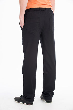 A person stands facing away, wearing the Bob Spears Pull On Pant, which features an elastic waist and back pockets. The comfortable pants appear to be made of a soft fabric and are paired with an orange shirt. The person’s hands are in their pockets, and they are wearing black sneakers with white soles. The background is plain white.