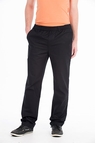 A person is standing against a plain white background, wearing a bright orange T-shirt and the Bob Spears Pull On Pant in black, with their hands inside the pants pockets. The comfortable pull-on pants also feature an elastic waist. They are wearing black sneakers with white detailing, though their face and upper part of the head are cropped out of the image.