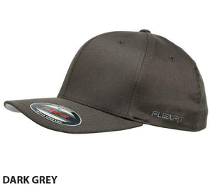 The FlexFit Worn By The World Cap is a dark grey, fitted design with a curved visor. It boasts style and comfort, featuring a small Flexfit logo on the side and a sticker on the visor that indicates the brand and size. The background is white.