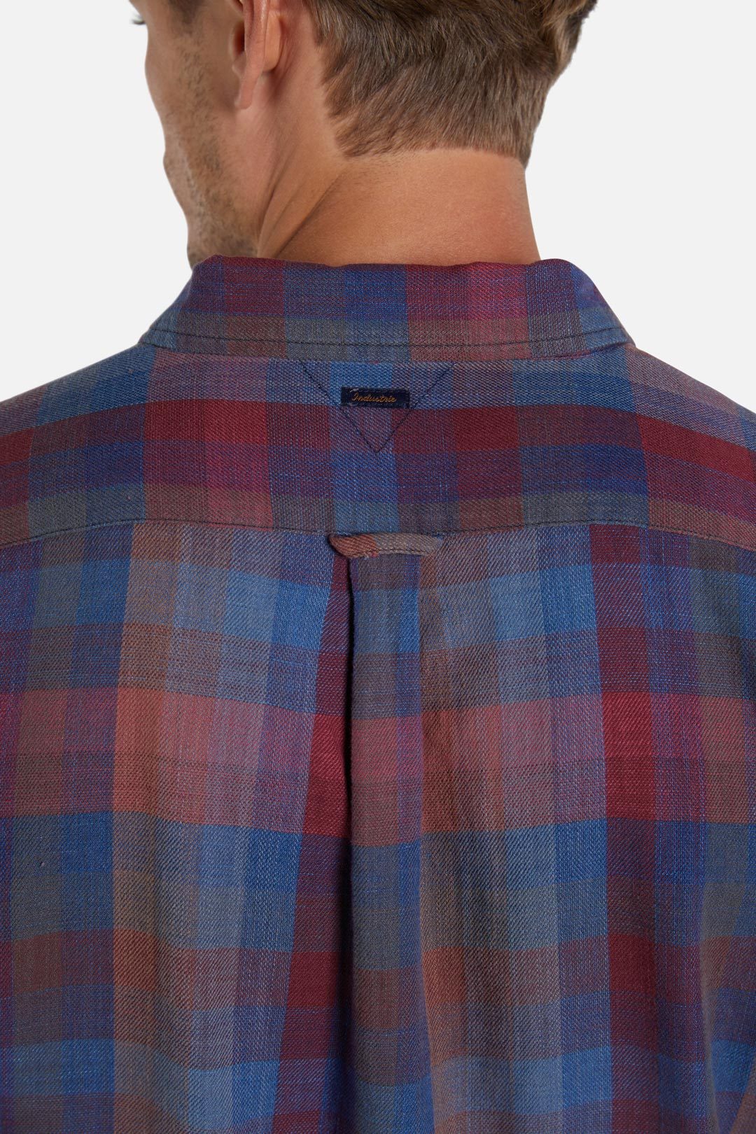 A person is shown from the back, wearing the Industrie The Harlow Shirt, a lightweight plaid shirt featuring hues of blue, red, and purple. The long sleeves and button front add to its classic look. It also has a collar and a box pleat detail at the center of the back. The person's hair is short, and the background is plain white.