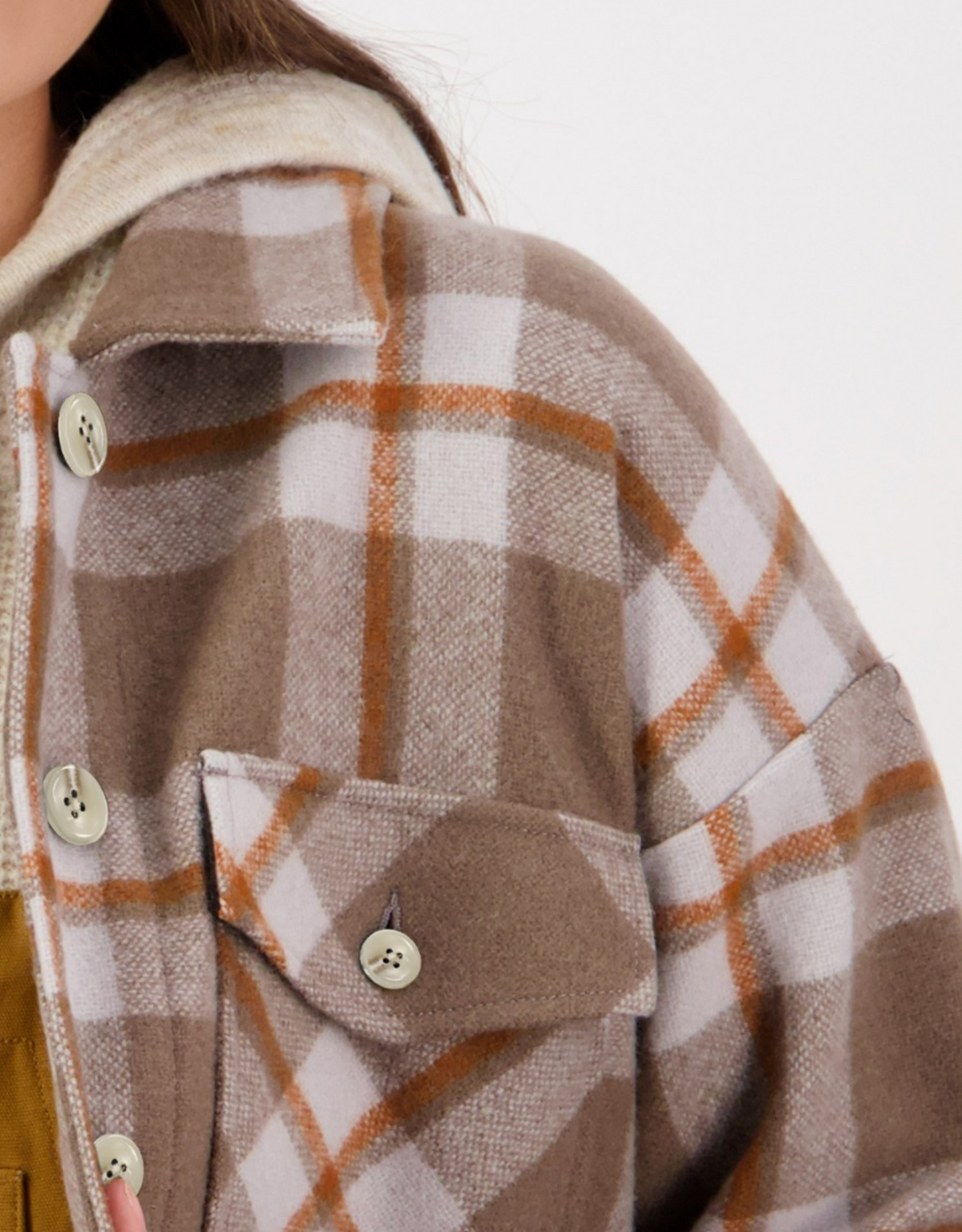 Close-up of a person wearing a plaid coat with large buttons and a pocket on the chest, featuring a pattern of brown, beige, and white squares. Underneath the coat, you can see the Swanndri Anchorage Wool Shirt Jacket in a light color.