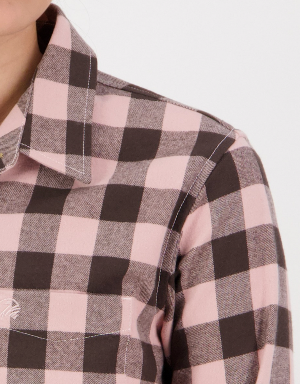 Close-up of a person wearing a Swanndri Women's Taranaki Tailor Shirt in pink and black checks, made from 100% cotton with a pointed collar and visible stitching, capturing the upper shoulder and part of the collar against a white background.