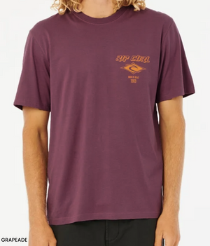 A person in a relaxed fit, purple Rip Curl Fade Out Icon Tee with an orange chest logo pairs their wavy hair with black organic cotton pants for a casual look.