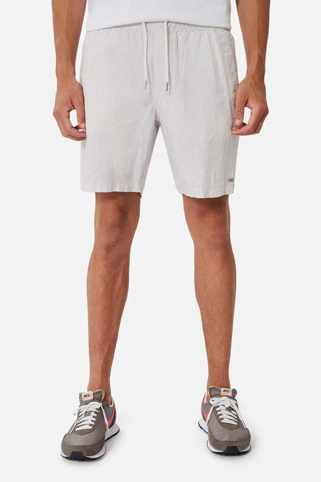 A person in Industrie The Elio Short, light gray with a drawstring and elastic waist, paired with sneakers. Crafted from a linen-cotton blend, only the lower body is visible against a plain background.