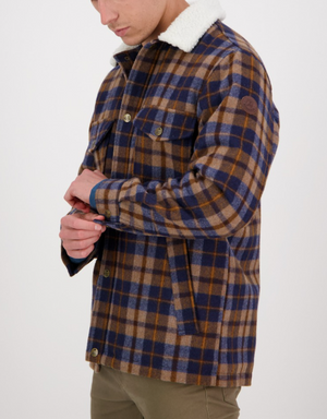 A man in olive green pants buttons the cuff of his Swanndri Kaituna Sherpa Lined Jacket—a brown, blue, and beige plaid piece with a white sherpa collar and cozy sherpa lining. Only the lower part of his face is visible.