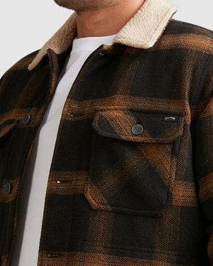 A person wears the Billabong Barlow Sherpa Jacket, featuring a black and brown plaid design, cream sherpa collar, and front flap pockets with metal snaps, over a white shirt. The image shows only the upper torso.