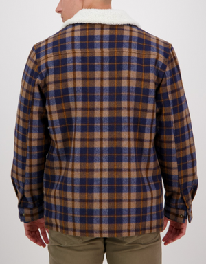 A person is shown from the back wearing the Swanndri Kaituna Sherpa Lined Jacket in blue, brown, and beige plaid with a white sherpa collar. They are also wearing khaki pants and have their hands relaxed at their sides.