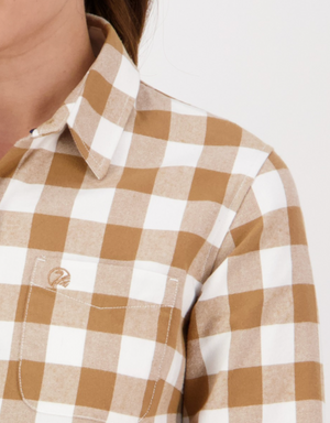 Close-up of a person wearing the Swanndri Womens Taranaki Tailor Shirt in tan and white check flannel, featuring a tailored fit, collar, front pocket with embroidered logo, and crafted from 100% cotton. Part of neck and shoulder visible.