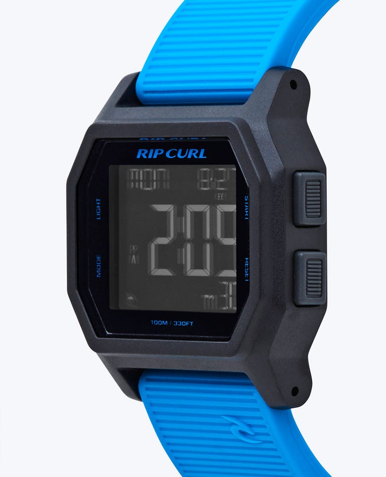 The Rip Curl Atom Digital Watch is waterproof, featuring a rectangular black case with blue accents and a blue textured strap. It displays time and date, and includes side buttons for light and mode functions.
