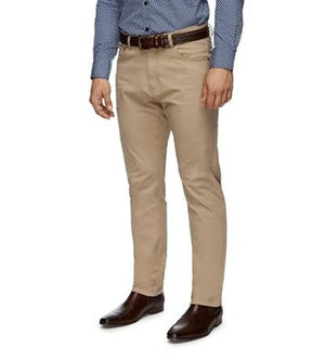 A person wearing a blue patterned shirt, beige City Club Austin Road Pant, and dark brown leather shoes stands casually with hands at their sides. The image focuses on the lower half of the body, showcasing the stylish pants and shoes.