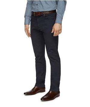 A person wearing a blue patterned shirt, City Club Austin Road Pant in dark blue, a brown braided belt, and brown leather shoes stands facing the camera. Only the person’s torso to feet are visible.