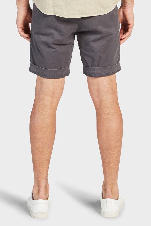 Rear view of a person wearing the dark gray Academy Brand Cooper Chino Shorts, rolled up at the hem, paired with a beige shirt and white sneakers. The person stands with their legs slightly apart against a plain, light-colored background.