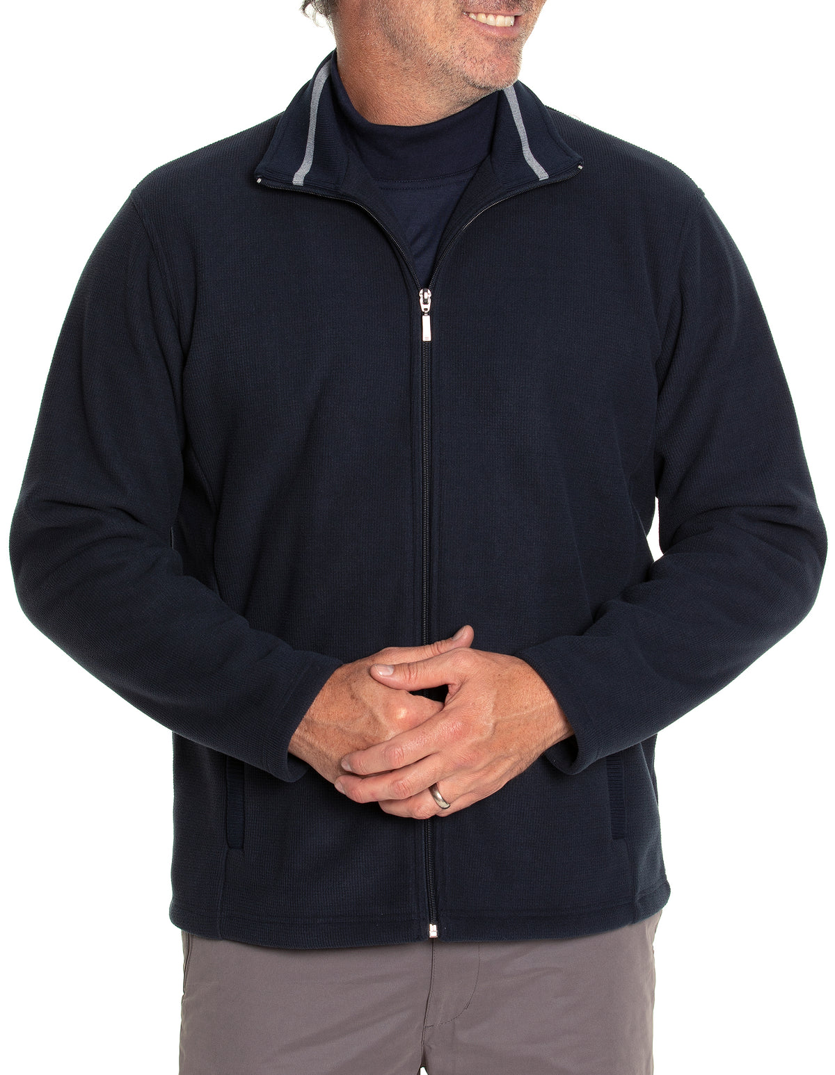 A man is standing with his hands clasped, wearing a navy blue Breakaway Stellan Jacket with a dark shirt underneath. The jacket features a stand-up collar with a light grey inner lining. He is dressed casually and smiling, although his face is not fully visible.