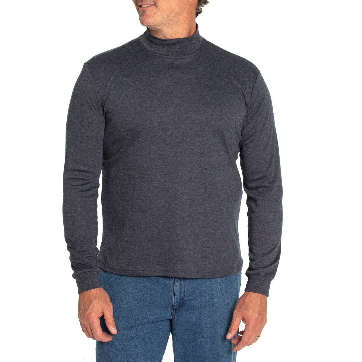 A man in a dark gray Breakaway Skivvy, made from a polyester-cotton mix, paired with blue jeans, stands against a white backdrop. He gazes to the side, lightly touching his shirt's edge, embodying effortless winter style.