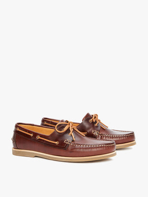 The RM Williams Hobart Boat Shoe is a pair of brown yearling leather boat shoes with tan laces and stitching, displayed on a white background. They feature a durable rubber outsole and visible side eyelets for the laces.