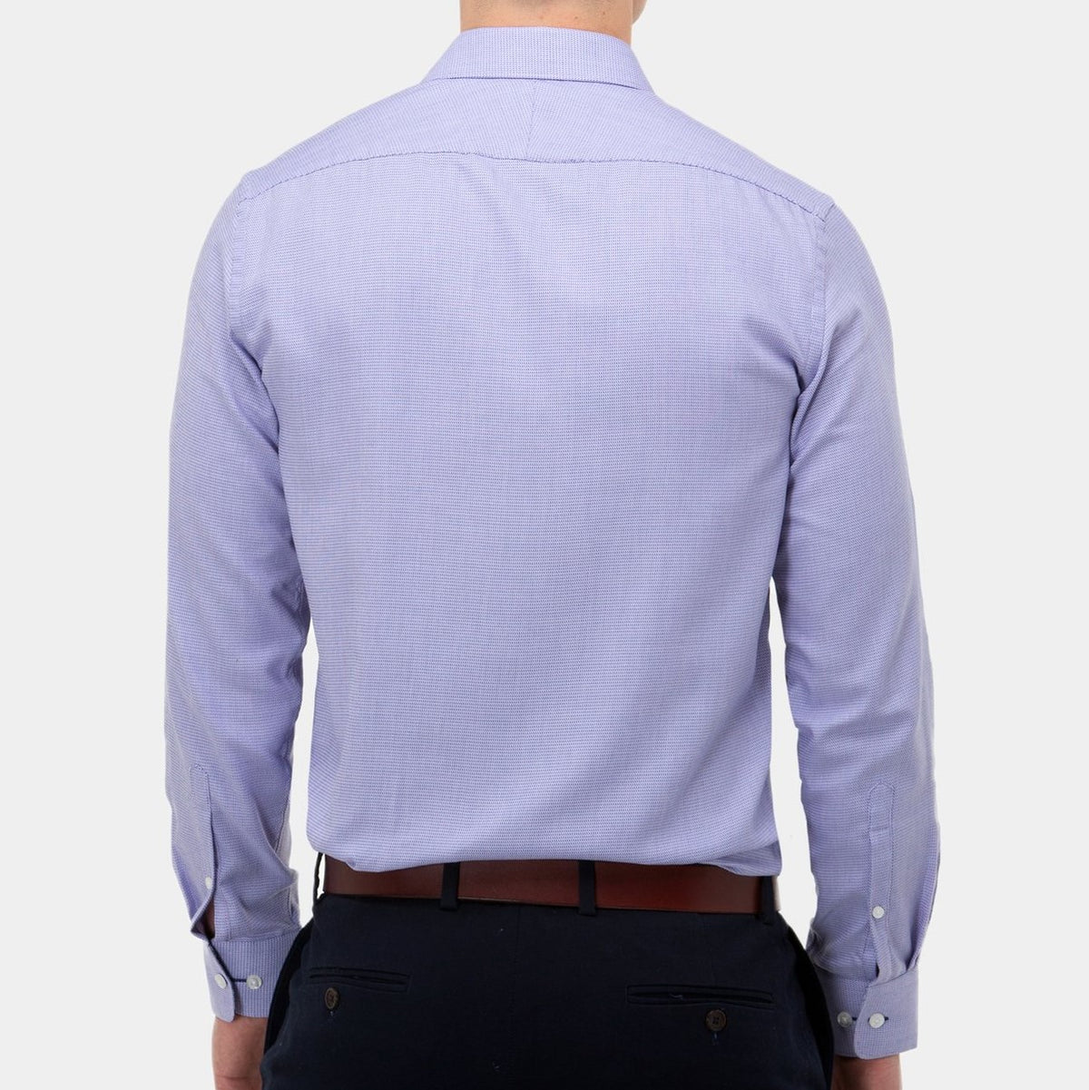 A person wearing a light blue, long-sleeved Brooksfield Micro Textured Shirt and dark pants is shown from the back. The stylish shirt is tucked into the pants, which have a brown belt. The background is plain and white.