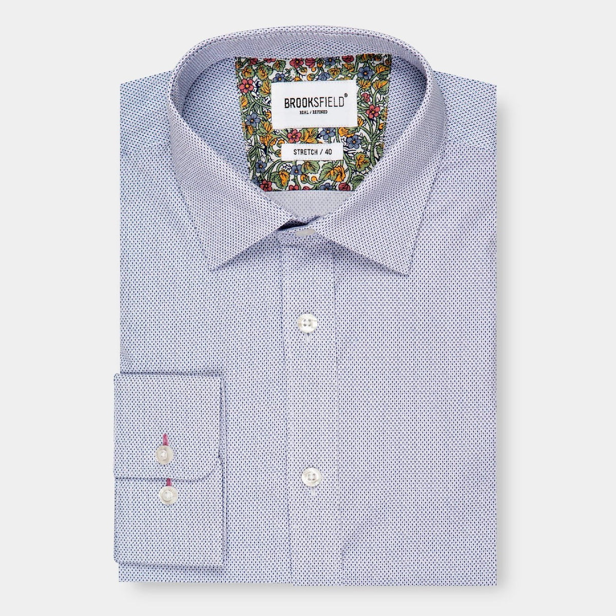 A neatly folded Brooksfield Stretch Print Shirt, long-sleeve and button-up in light blue with a subtle textured pattern. The inner collar and cuffs feature a colorful floral design. The tag reads "BROOKSFIELD" and "STRETCH / 40". This regular fit shirt is displayed on a plain white background.