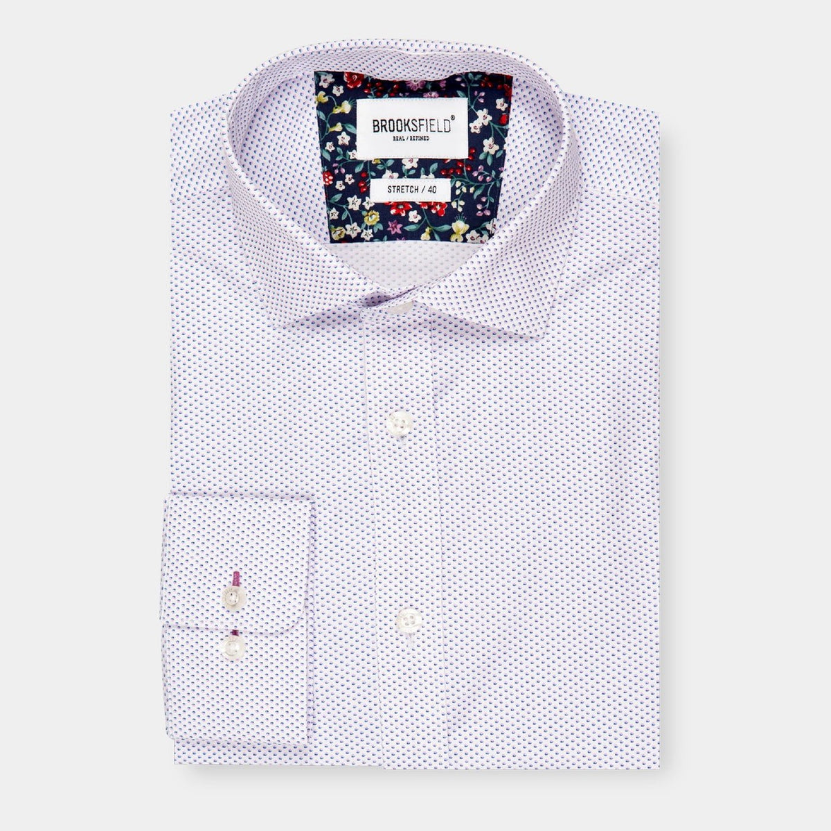 A neatly folded Brooksfield Stretch Print Shirt with a subtle purple dotted pattern displayed against a white background. The inside of the collar features a contrasting floral pattern. The label reads "Brooksfield - Non Iron - STRETCH - A9". This stylish shirt seamlessly combines comfort and elegance.