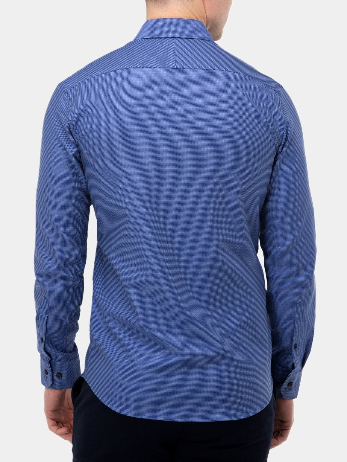 A person seen from behind, wearing a Brooksfield Luxe Textured Shirt. This slim fit, long-sleeved, button-up blue shirt features small checkered patterns and buttoned cuffs. Made from 100% cotton, the stylish shirt stands out against a plain, light background.