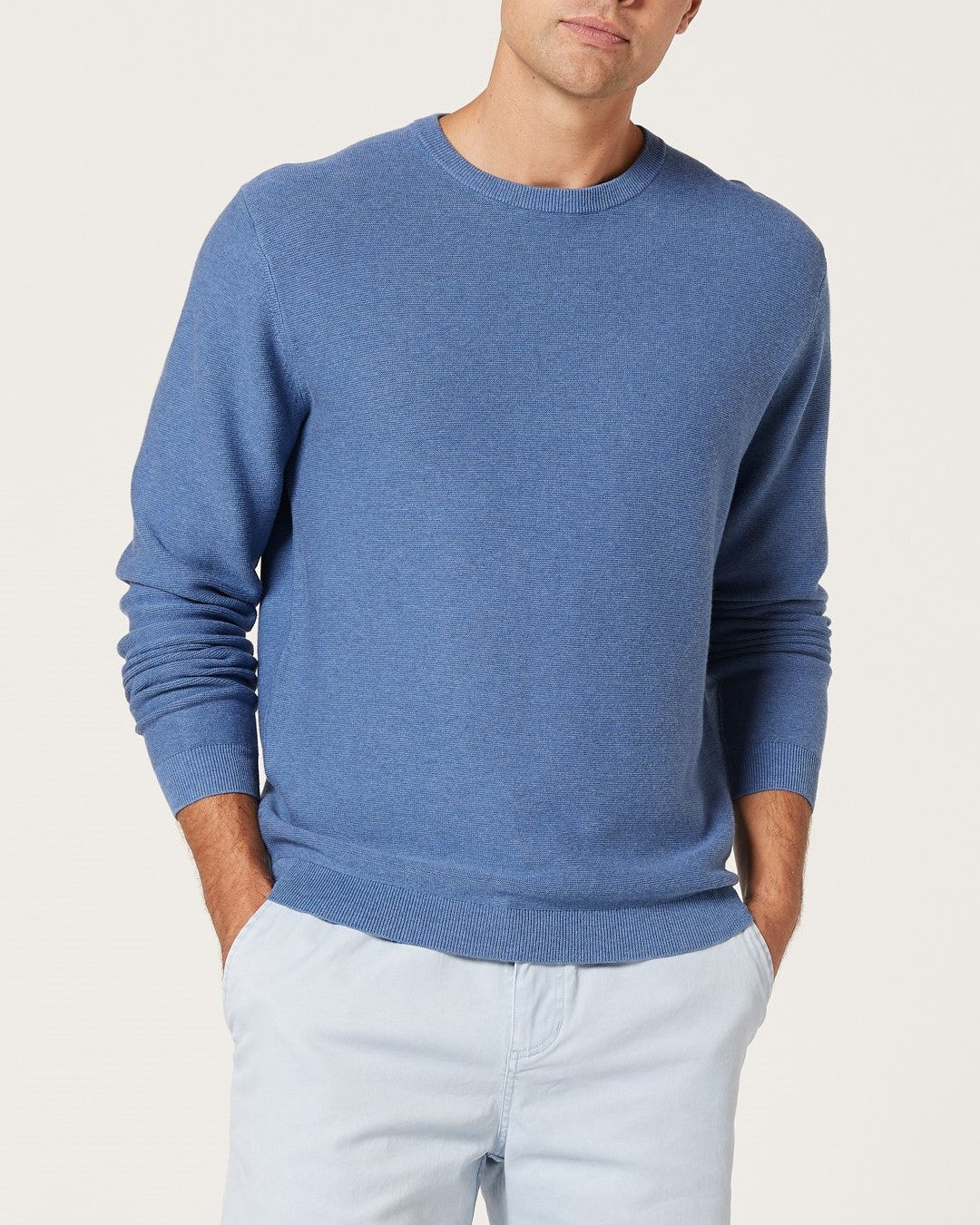A man wears the Blazer Mason Cotton Crew Neck in denim with light-colored pants, standing with his hands in his pockets against a plain background.