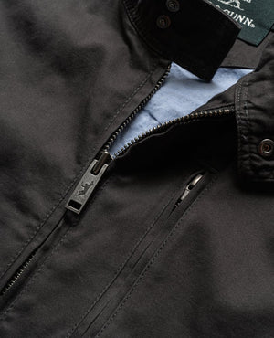 Close-up of a black Rodd & Gunn Armitage Jacket shows a partially open zipper, revealing light blue lining. The jacket, made from premium Australian cotton, features intricate stitching and a collar with button accents.