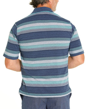 A man in a Breakaway Otto Kinnersly Jersey Polo with horizontal green, blue, and gray stripes stands with his back facing the camera. He is wearing blue pants against a plain white background. The classic collar of the polo adds a touch of refinement to his relaxed look.