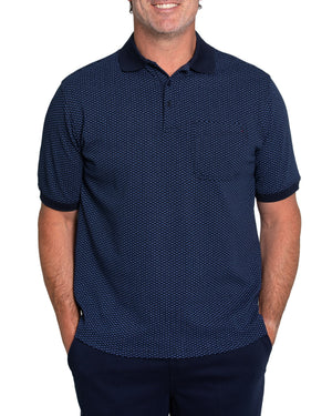 A person stands with hands in pockets against a white background, wearing the Breakaway Diamond Micro Prima Polo, a navy blue casual shirt with a classic collar and dark blue sleeve cuffs, featuring a subtle small repeated design.