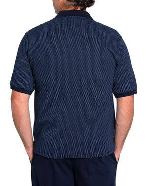 Rear view of a person wearing a Breakaway Diamond Micro Prima Polo, featuring a dark blue pattern and classic collar, paired with dark trousers. Their hands are tucked into their pockets against a crisp white background.