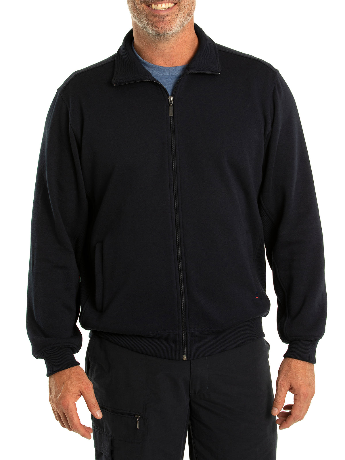 A man is wearing the Breakaway Zed Snowy Mt Fleece Full Zip in black, featuring a cosy fleece lining. He pairs it with a blue shirt and black pants. Smiling with his arms relaxed at his sides, the zip-up jacket boasts a collar and two front pockets. The background is plain white.