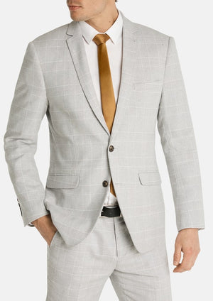 Man wearing the Connor Sorrento Slim Suit Jacket in light grey plaid over a white dress shirt and gold tie, standing with one hand in his pocket against a plain white background.