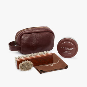 The RM Williams Mini Travel Care Kit includes a burgundy leather pouch with "R.M. Williams" embossed in the center, a tin of chestnut boot polish, a wooden brush with bristles, a smaller round brush, and a square leather cloth featuring a printed bull logoβperfect for caring for your R.M. Williams boots.