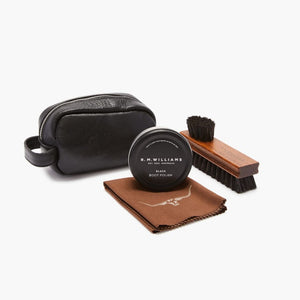 The RM Williams Mini Travel Care Kit, perfect for maintaining the pristine look of your R.M. Williams boots, includes a black leather pouch, a tin of R.M. Williams black boot polish, a wooden-handled brush with brown bristles, and a brown polishing cloth with the logo. All items are arranged neatly against a white background.