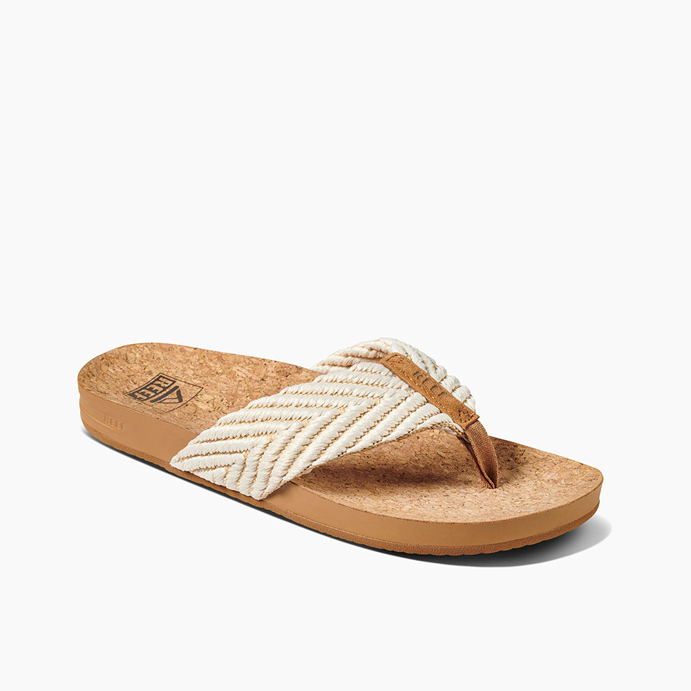 The REEF Cushion Strand sandal features a single cork design with a woven strap in shades of white, beige, and light brown. It includes a brown footbed with enhanced arch support and an embossed logo on the side of the sole. The sandal's casual, beachy style is perfectly complemented by its cushion bounce midsole for added comfort.