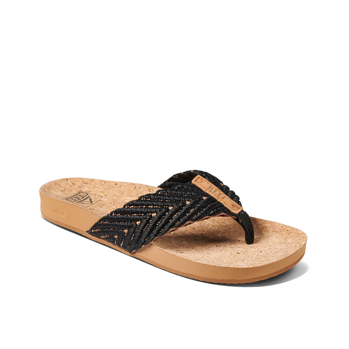 The REEF Cushion Strand is a black woven flip-flop sandal featuring a cushion bounce midsole, cork footbed, and tan sole. Its zigzag-patterned straps include a small tan tag. This stylish sandal is displayed against a white background.