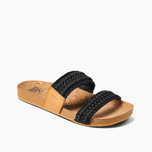 The REEF Cushion Vista Thread is a stylish sandal featuring a cork footbed and two wide, black woven fabric straps. Its light brown sole is enhanced with an EVA foam compound for added comfort. This minimalist, contemporary design is perfect for casual wear.
