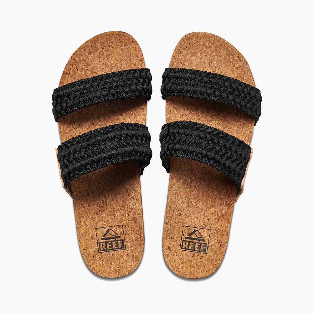 A pair of REEF Cushion Vista Thread sandals with cork soles and two black woven straps across each foot. The simple, natural design features a comfortable cushion bounce midsole, and the brand logo "Reef" is printed on the soles near the heels.