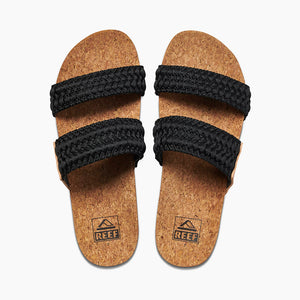 A pair of REEF Cushion Vista Thread sandals with cork soles and two black woven straps across each foot. The simple, natural design features a comfortable cushion bounce midsole, and the brand logo "Reef" is printed on the soles near the heels.