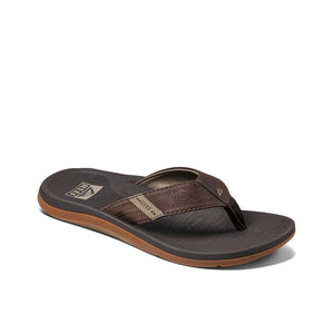 The REEF Santa Ana men's flip-flop sandal, in a blend of brown and tan, is showcased against a white background. This sandal boasts a textured strap and sole, comfortable thongs, a branded logo near the heel, and arch support for enhanced comfort.