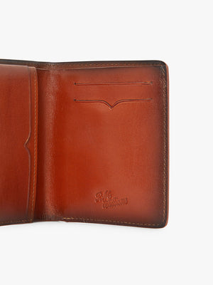 The RM Williams Urban Bi-Fold is a brown full grain leather wallet with two card slots, embossed "R.M. Williams" logo on the lower right, smooth finish, and visible edge stitching.