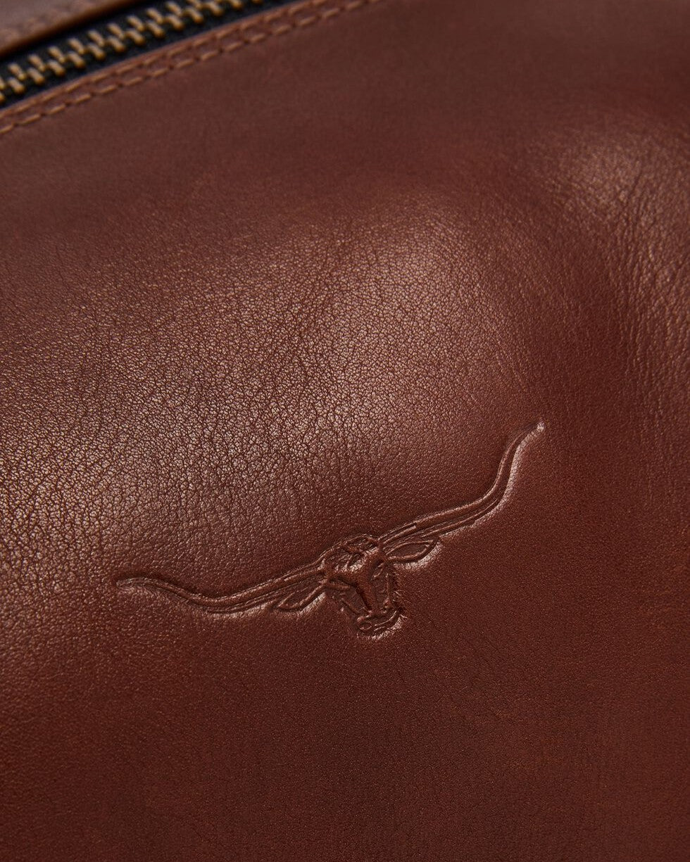Close-up of brown leather on the RM Williams Leather Ute Bag, showing an embossed longhorn cattle head design and a brass zipper visible at the top edge.