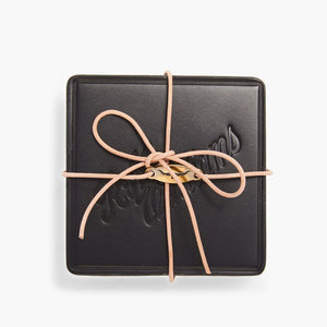 The RM Williams Heritage 6 Pack Coaster Set features a black square leather case with embossed text on the lid, tied with a beige leather cord in a bow, showcasing fine Australian craftsmanship against a white background.