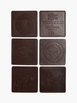 The RM Williams Heritage 6 Pack Coaster Set includes six brown leather coasters made in Australia, embossed with designs in two vertical columns featuring multiple RM Williams logos, circular motifs, and horse imagery.