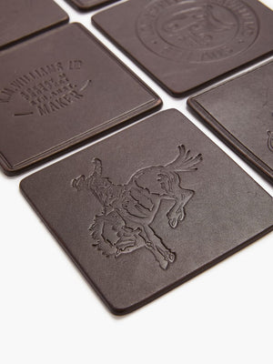 The RM Williams Heritage 6 Pack Coaster Set features embossed brown leather coasters with designs such as a cowboy on a bucking horse, artfully arranged in a grid. Made in Australia.