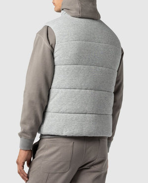 A person is seen from the back, wearing a gray hooded sweatshirt and gray pants, paired with the Rodd & Gunn Jackett Island Vest featuring high-loft synthetic insulation, against a plain light gray background. Their hood is down.