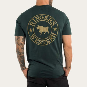 A man wears the Ringers Western Signature Bull Classic T-shirt, a dark green 100% cotton casual tee with a bull silhouette logo encircled by "Ringers Western" and stars on the back. The crew neck shirt pairs well with his tattooed arm and black pants as he stands facing away.