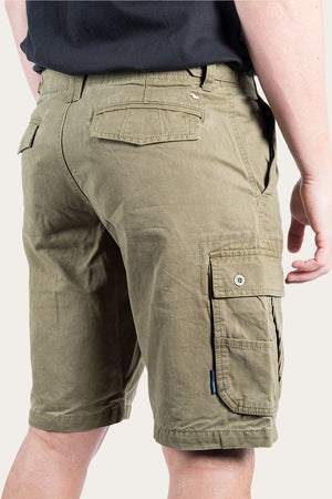 A person wearing Ringers Western Gawler Cargo Shorts in olive green, made from 100% cotton, paired with a black shirt. The shorts feature multiple pockets, including buttoned flap pockets on the sides and back. The individual is shown from the waist down, with their right hand partially visible at their side.